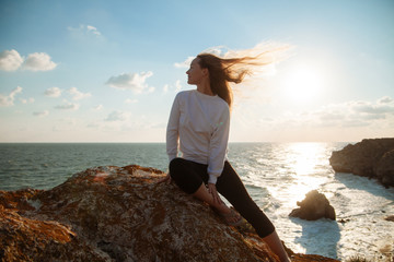 A young girl sitting on a rock on the background of the sea coast. The girl smiles and her hair fluttering in the wind