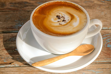 a cup of hot coffee with latte art and milk  foam, serving on old wooden table in day light