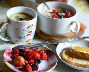 breakfast still life with oatmeal, seasonal berries, roasted toasts with lemon jam cup of tea spoon and knife