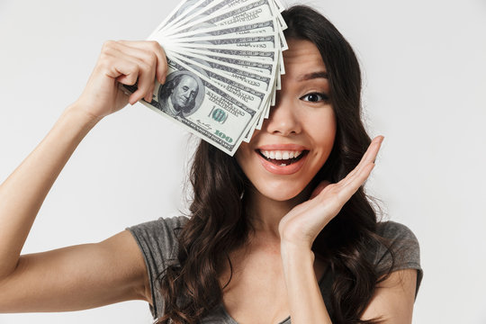 Image of positive brunette woman 20s dressed in basic clothes smiling and holding bunch of money bills