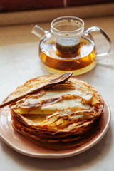 Stack of hot classic Russian thin pancakes. Rustic style. Traditional for the Russian pancake week - Maslenitsa. Tea pot in the background.