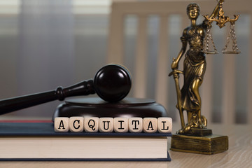 Word ACQUITAL composed of wooden dices. Wooden gavel and statue of Themis in the background.