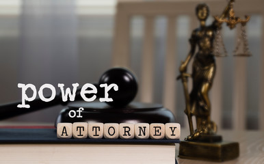 Words POWER OF ATTORNEY  composed of wooden dices. Wooden gavel and statue of Themis in the background.