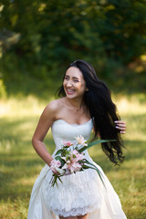 Young pretty brunette laughing woman in white wedding dress, walking outdoors