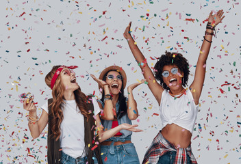 Three attractive young women cheering and smiling while standing against grey background