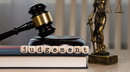 Word  JUDGEMENT composed of wooden dices. Wooden gavel and statue of Themis in the background.
