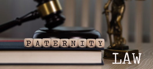 Words PATERNITY LAW  composed of wooden dices. Wooden gavel and statue of Themis in the background.