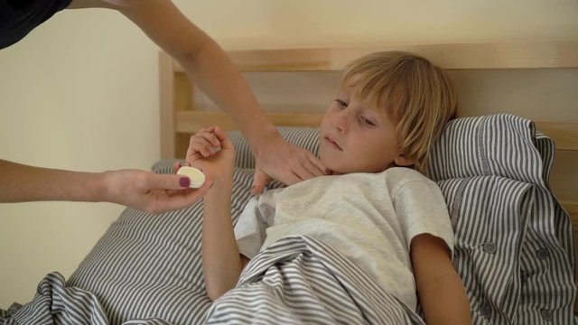 Superslowmotion shot of a sick little boy in a bed. Mother rubs boy's chest with ointment with essential oils. Baby flu concept