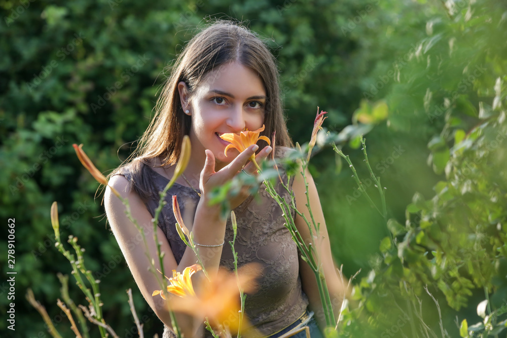 Wall mural happy young woman standing in a park near flowers, candid outdoor portrait of beautiful brunette