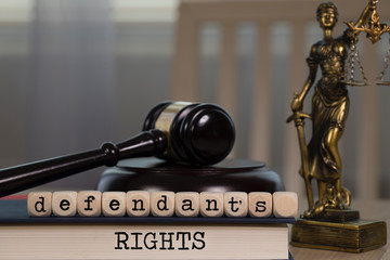 Words DEFENDANT'S RIGHTS composed of wooden dices. Wooden gavel and statue of Themis in the...