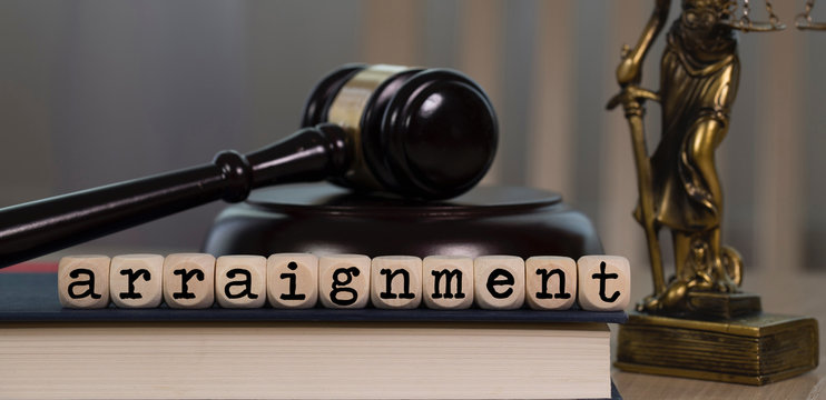 Word ARRAIGNMENT composed of wooden dices. Wooden gavel and statue of Themis in the background.