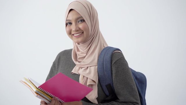 Beautiful veiled student carrying books and bag with smile looking the camera at isolated background