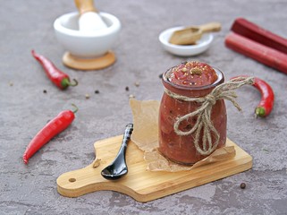 Spicy rhubarb chutney sauce in a glass jar on a gray background. Preserving, harvesting. Indian food.