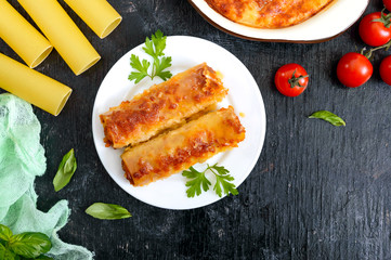 Stuffed cannelloni with bechamel sauce. Cannelloni pasta baked with meat, cream sauce, cheese on a black background. Top view, flat lay.