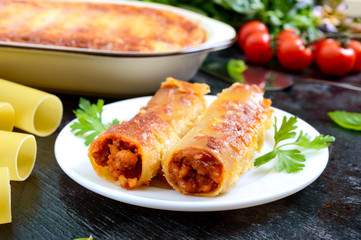 Stuffed cannelloni with bechamel sauce. Cannelloni pasta baked with meat, cream sauce, cheese on a black background