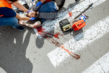 Ambulance worker with man in road vest applying emergency medical care to the injured bleeding...