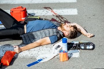 Injured bleeding man lying on the pedestrian crossing during the emergency care after the road accident
