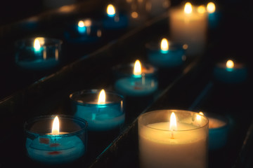 Closeup of rows of prayer candles burning in blue glass tealights in a church. Shallow depth of field.