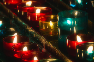 Closeup of rows of candles burning in multicolored glass tealights in a church. Selective focus.