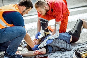 Ambluence workers applying emergency care to the injured bleeding man lying on the pedestrian...