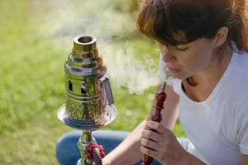 Young hipster woman smoking sisha (water pipe) within summer festival