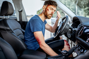 Fastened driver with deep bleeding injuries feeling shocked after the road accident inside the car