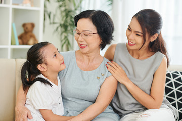 Asian family generation of three sitting on sofa smiling and talking to each other at home