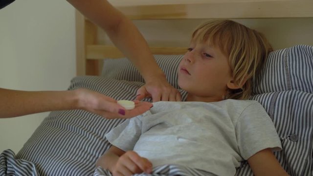 Sick little boy in a bed. Mother kisses him and rubs boy's chest with ointment with essential oils. Baby flu concept