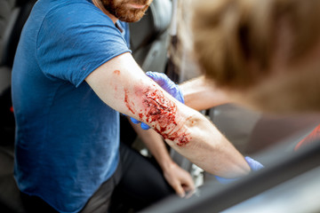 Ambulance worker examining injuries of a man sitting near the car after the road accident,...