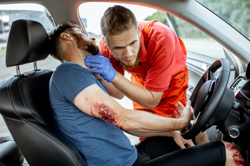 Medic examinig bleeding victim on the driver seat after the road accident, providing emergency...