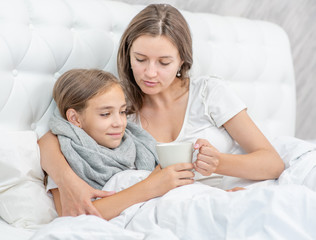 Obraz na płótnie Canvas Young mother taking care of sick daughter in bedroom and giving her cup of tea