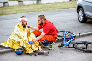 Ambluence worker covering injured man with thermal blanket, providing emergency care after the road...