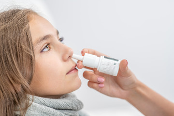 Mother using nose spray to cure her teen girl at home. Side view, empty space for text