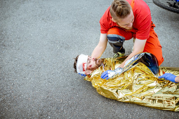 Ambluence worker covering injured man with thermal blanket, providing emergency care after the road...