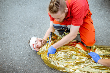 Ambluence worker covering injured man with thermal blanket, providing emergency care after the road accident