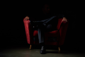 male businessman in a black suit sitting in red chair, black background, no faces visible, studio shooting
