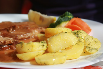Appetizing boiled potatoes with dill and meat decorated with carrots on a white dish.