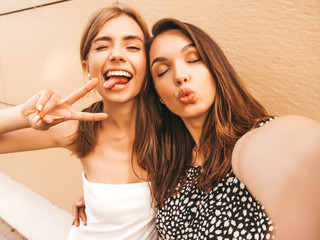 Two young smiling hipster women in summer clothes. Girls taking selfie self portrait photos on...