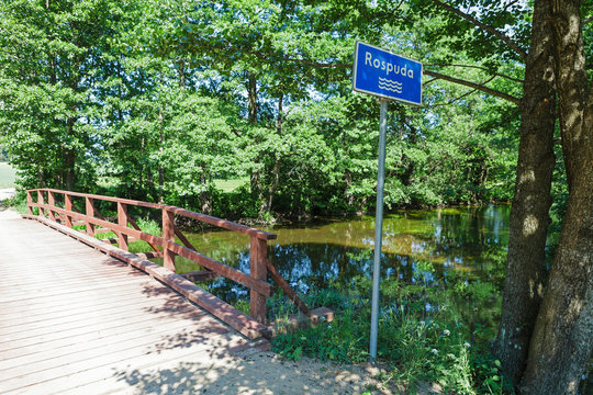 Blue sign with name of the river "Rospuda" by the wooden bridge, Poland