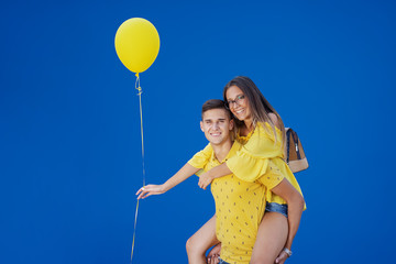 Happy smiling Caucasian teenage couple dressed in blue and yellow outfit having piggyback ride....