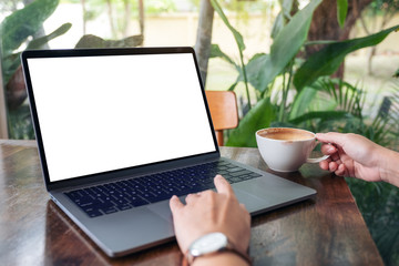 Mockup image of a woman using and touching laptop touchpad with blank white desktop screen while drinking coffee
