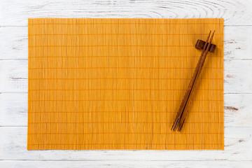 two sushi chopsticks with empty yellow bamboo mat or wood plate on white wooden Background Top view with copy space. empty asian food background