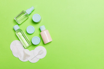Group of small bottles for travelling on green background. Copy space for your ideas. Flat lay composition of cosmetic products. Top view of cream containers with cotton pads