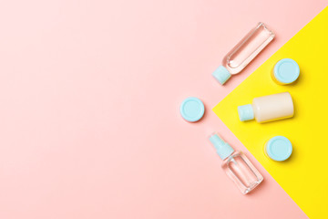 Top view of different cosmetic bottles and container for cosmetics on pink and yellow background. Flat lay composition with copy space