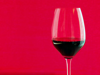 dark red wine in a glass on a red background.