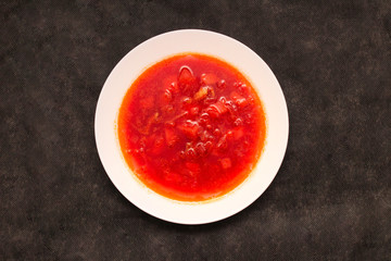 Flat top view vegetable beetroot soup, on the table. Borscht in a white plate on black canvas.