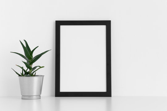 Black frame mockup with a aloe vera in a pot on a white table. Portrait orientation.