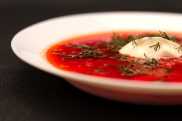 Bowl of beet root soup borscht with sour cream and greens isolated on black canvas with dark background