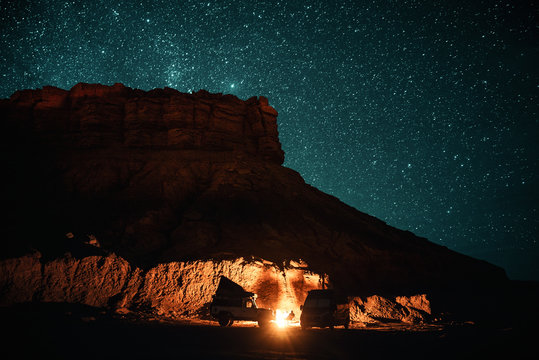 Lagerfeuer umstellt von einem Gel&auml;ndewagen und Campervan in der Nacht bei erg chebbi bei merzouga in Marokko unter einem Sternenhimmel 