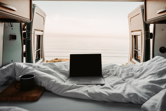 Bett im CAmperVan mit einem Notebook und ge&ouml;ffneten T&uuml;ren mit Bilck auf das Meer 